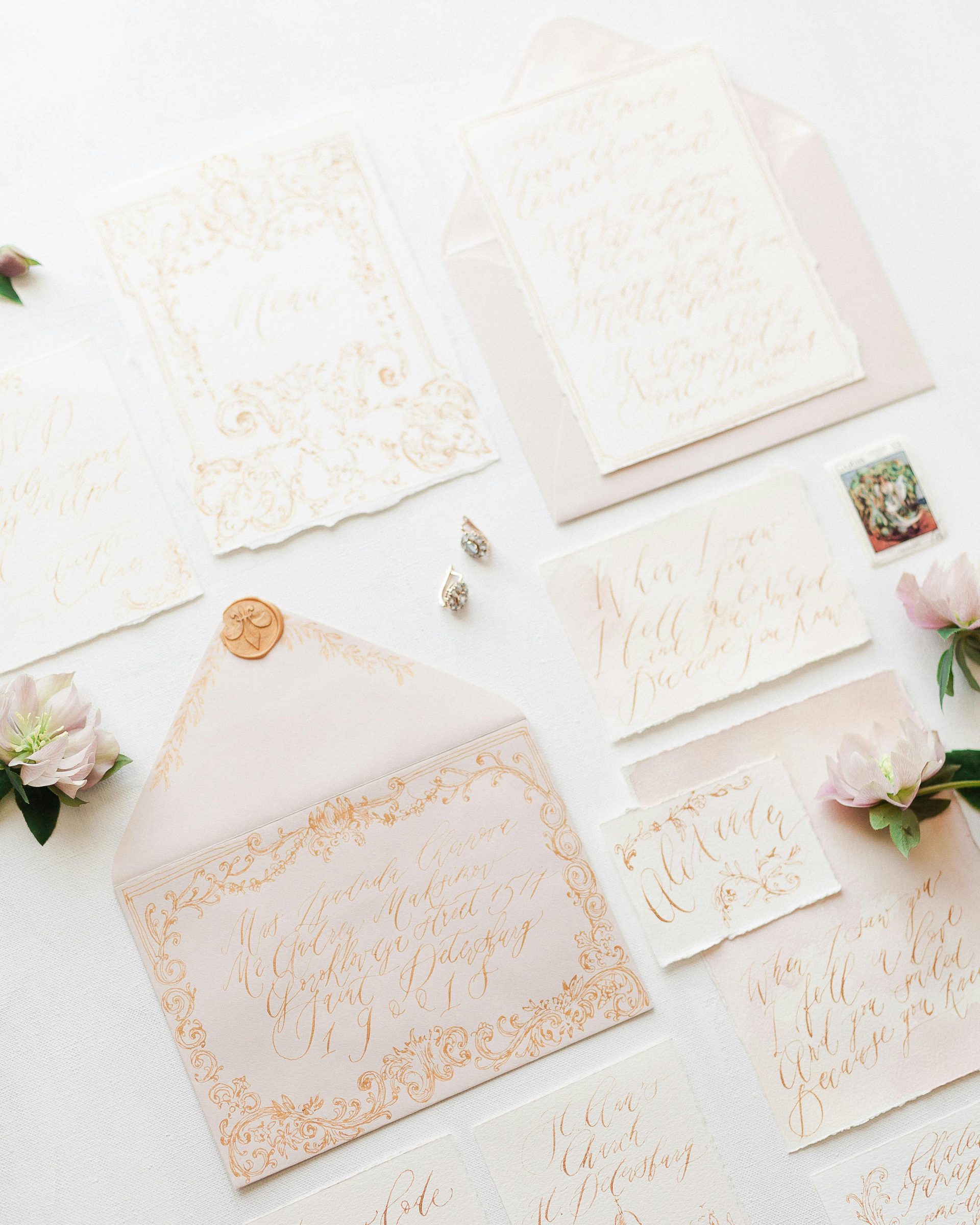 Ornate wedding invitations and envelopes in a flat lay with floral accents.